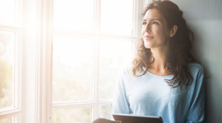 Thoughtful young woman holding digital tablet by window