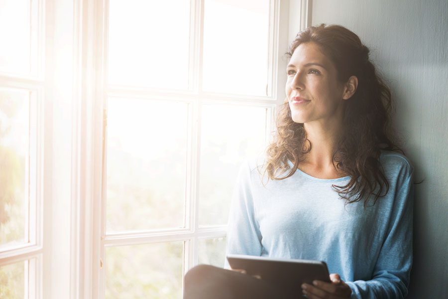 Thoughtful young woman holding digital tablet by window