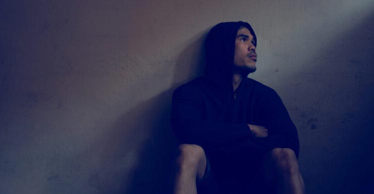 Depressed and hopeless asian man sitting alone after using drugs sitting on the floor. Drugs addiction and withdrawal symptoms concept.