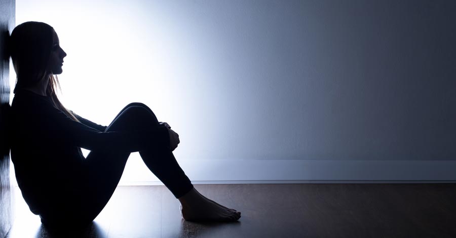 silhouette of a sad woman sitting on the floor against a wall