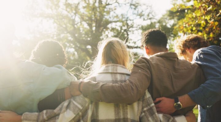 A group of friends stand outdoors with their arms around each other, symbolizing unity, support, and community in recovery.