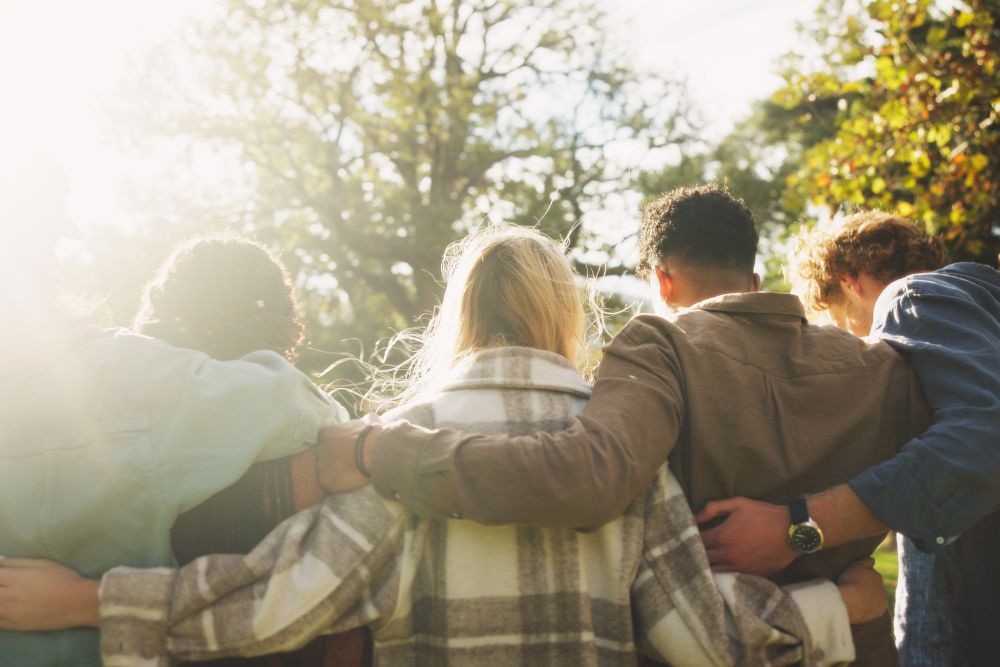 A group of friends stand outdoors with their arms around each other, symbolizing unity, support, and community in recovery.