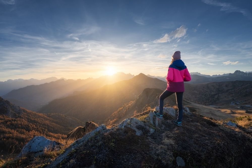A person stands on a mountain overlook at sunrise, facing the horizon with a sense of reflection, strength, and calm.