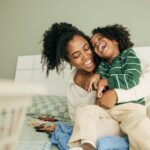 Ivory Plains - Use Laughter to Support Better Health. A woman and a child sit on a couch laughing with one another.